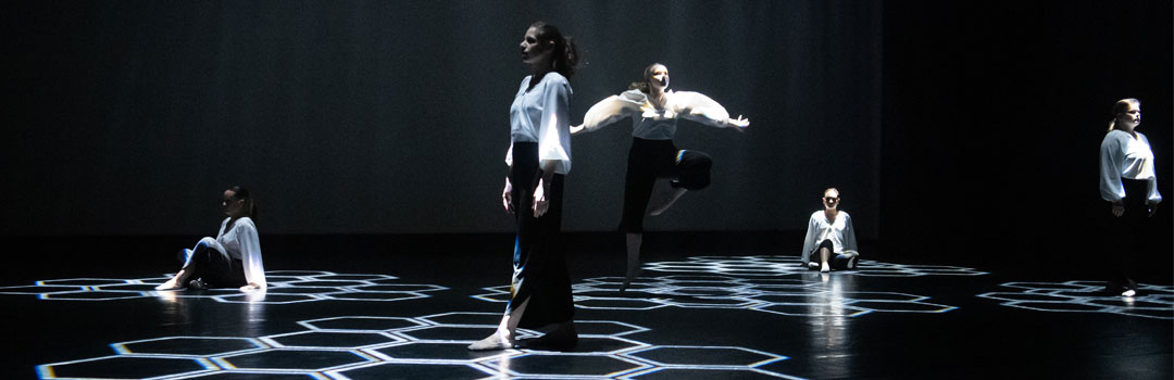 Contemporary dance performance featuring multiple dancers in flowing attire against a dark background with geometric patterns of light.